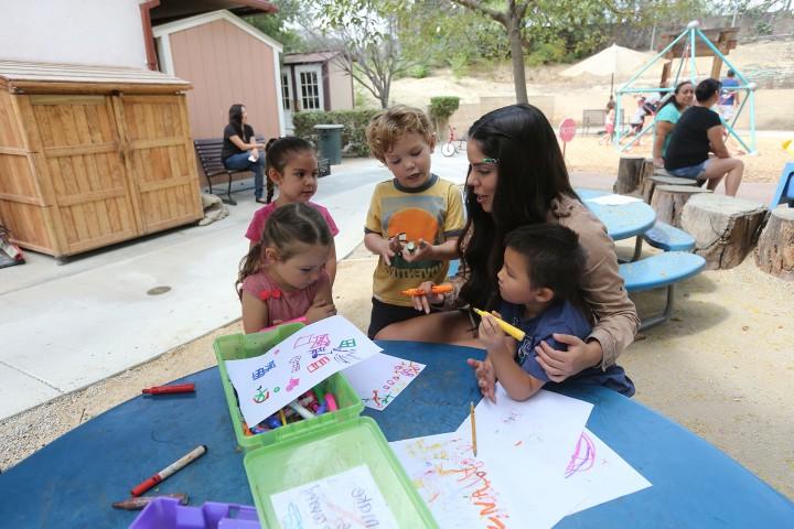 An adults sits with three children at a table outdoors.